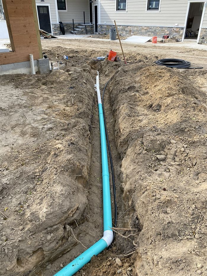Trench with blue PVC pipes installed, likely for plumbing or drainage, at a construction site.