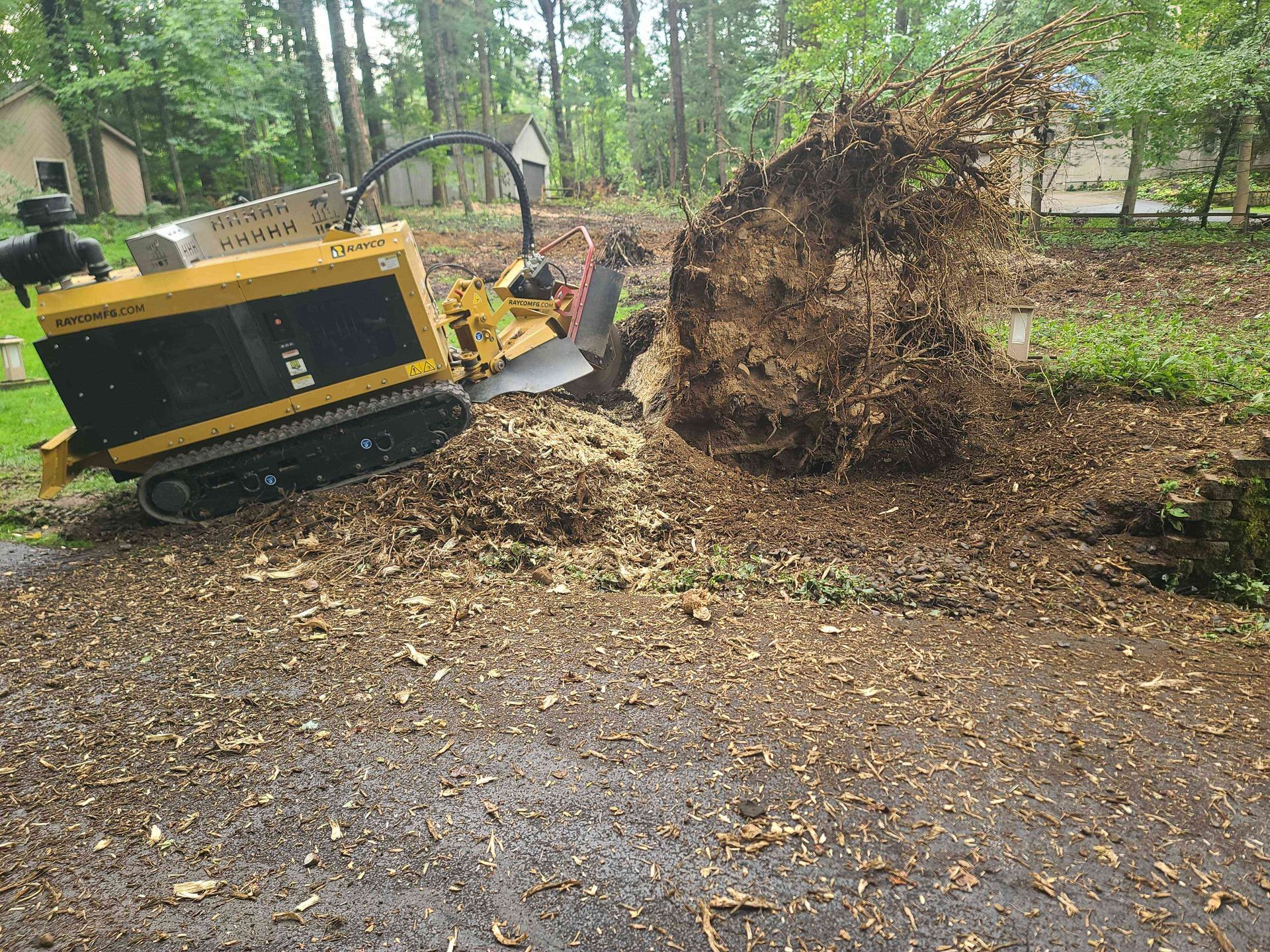 A large tree stump is being removed by a machine in a driveway.