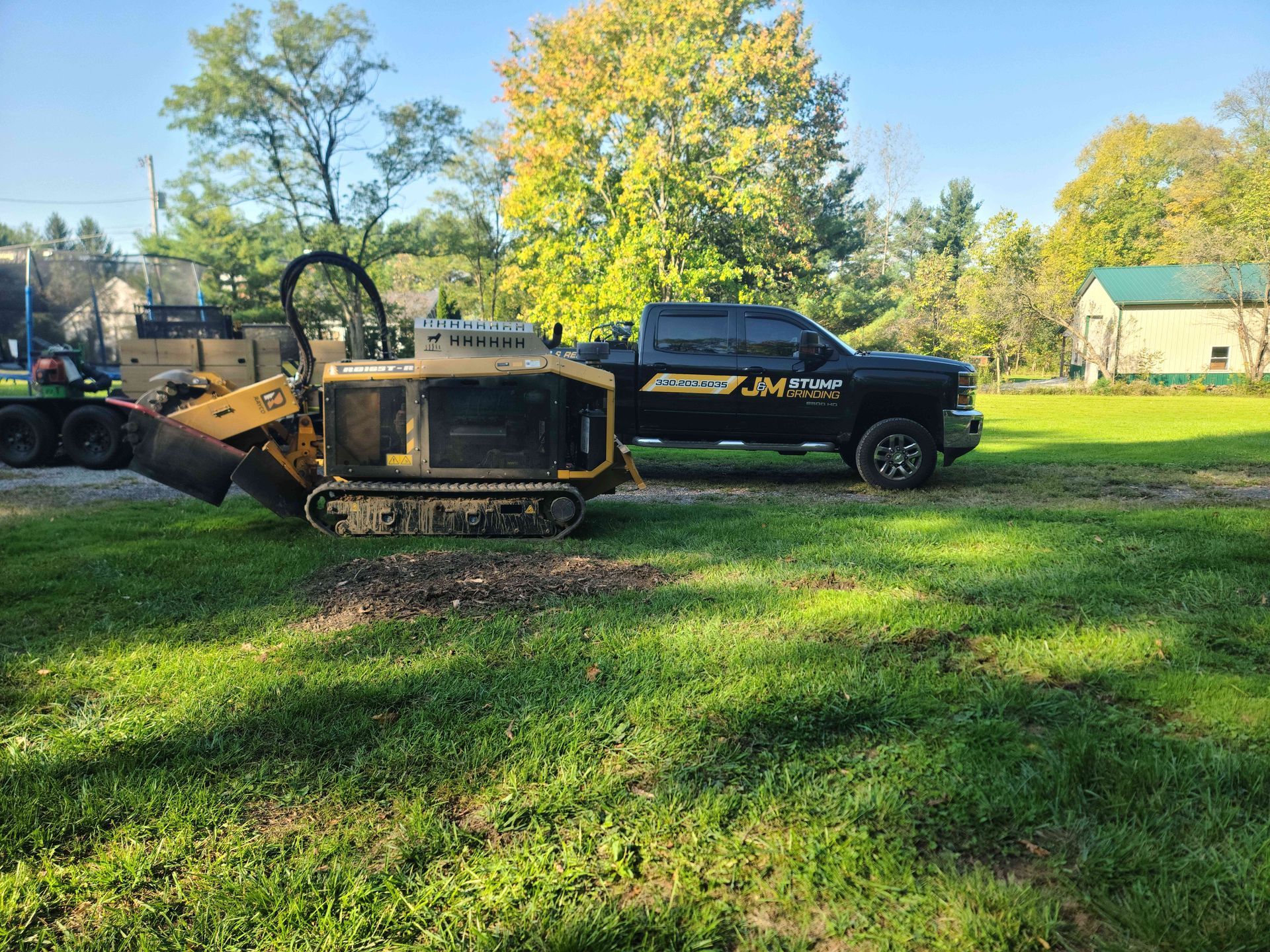 A truck is towing a stump grinder in a grassy field.