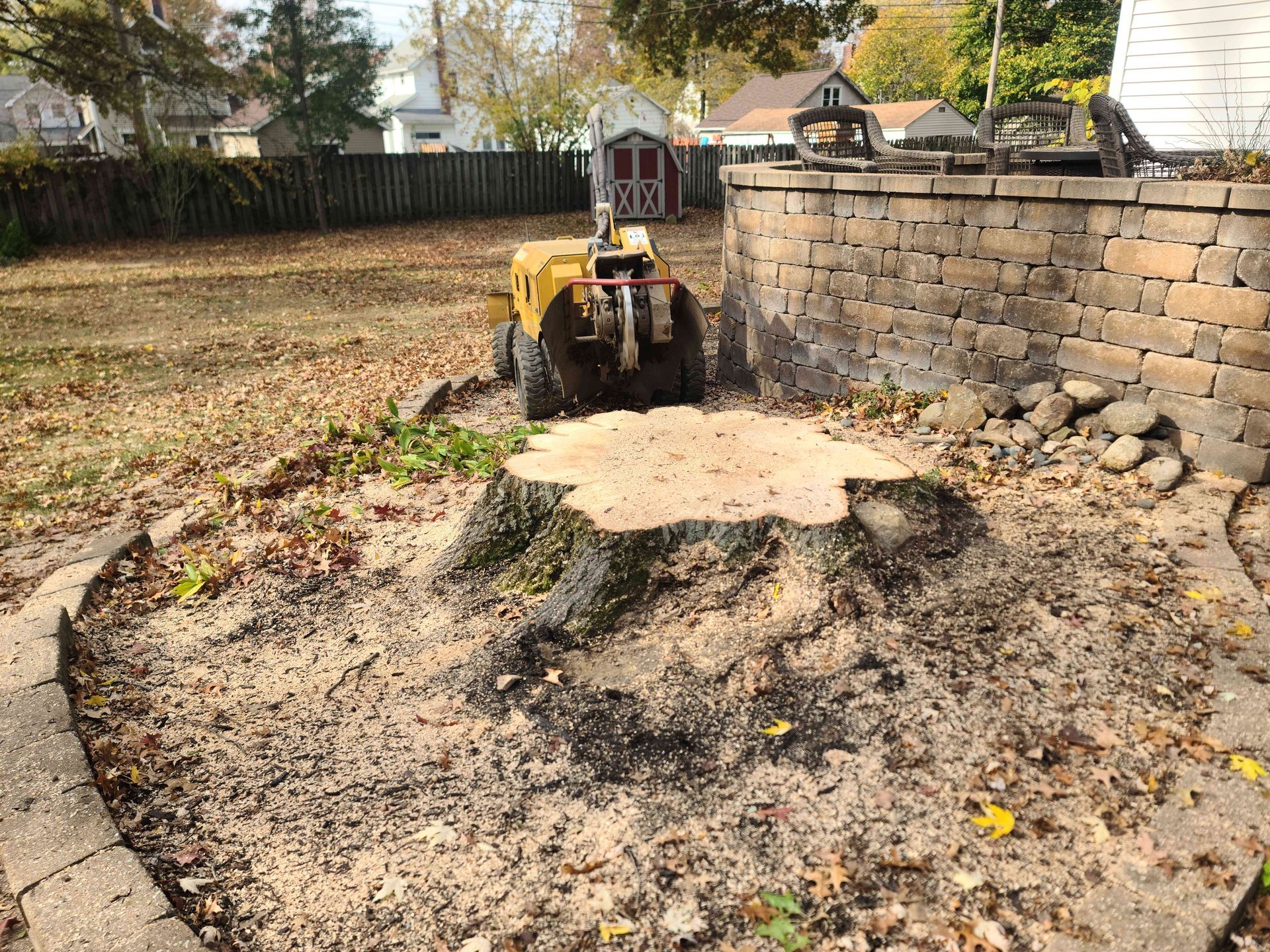 A tree stump is being removed by a machine in a backyard.