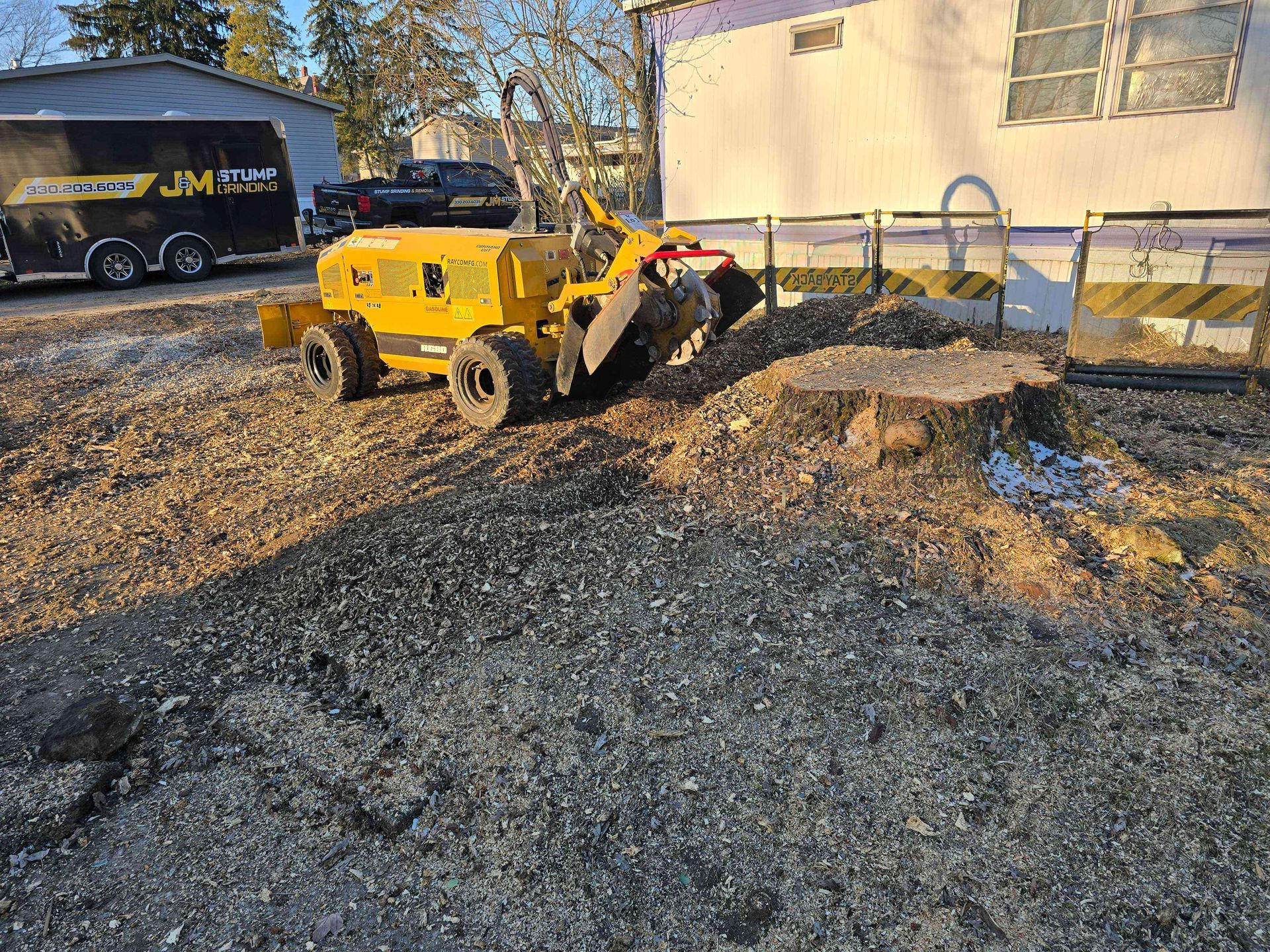 A yellow tractor is cutting a tree stump in a dirt field.