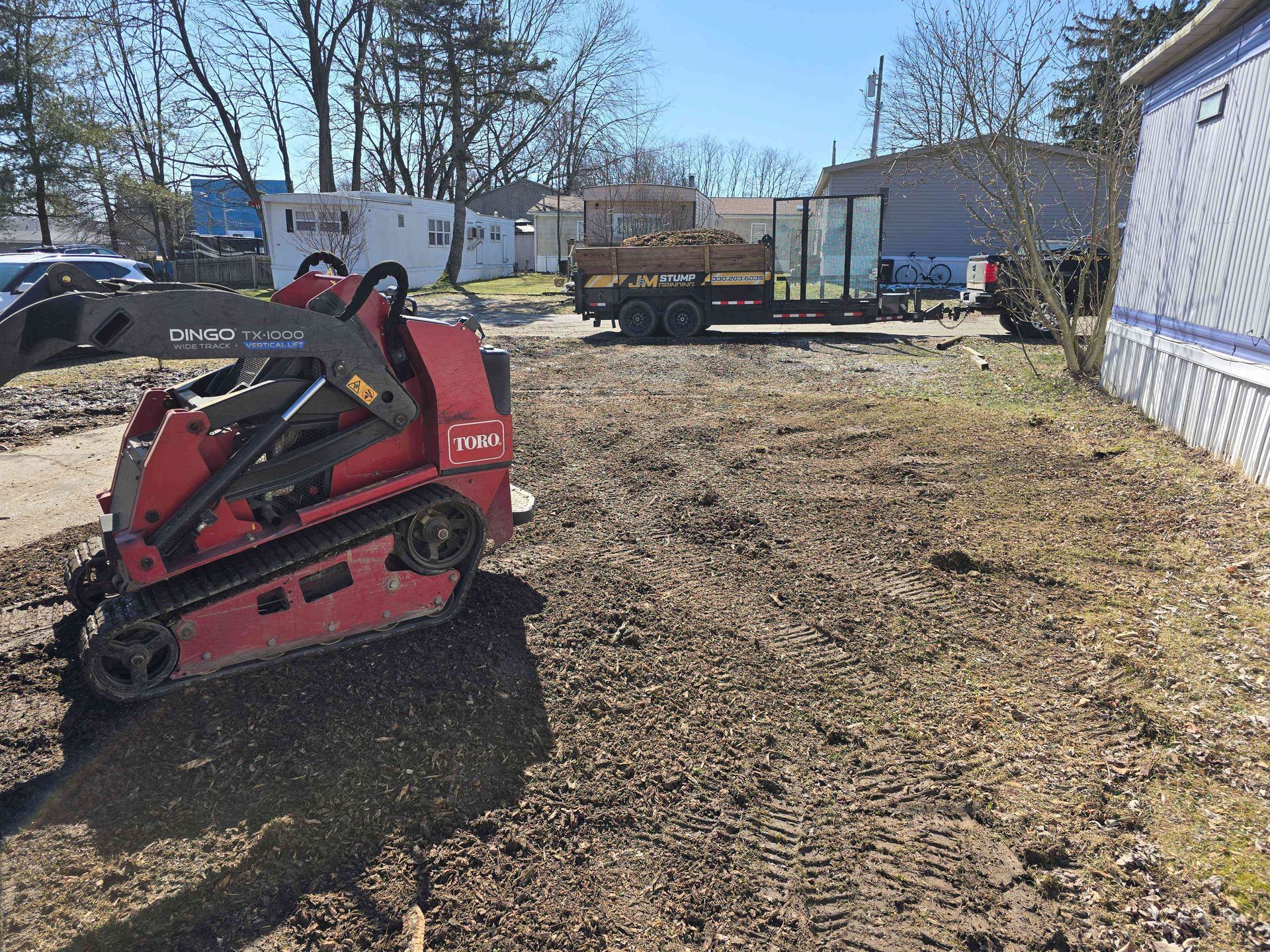 A red tractor is parked in a dirt field next to a trailer.