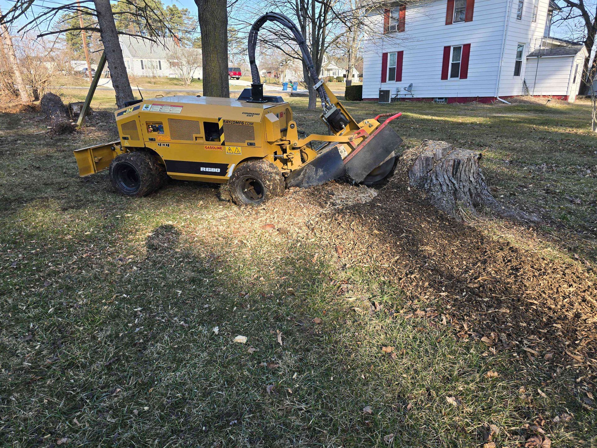 A yellow stump grinder is cutting a tree stump in a yard.