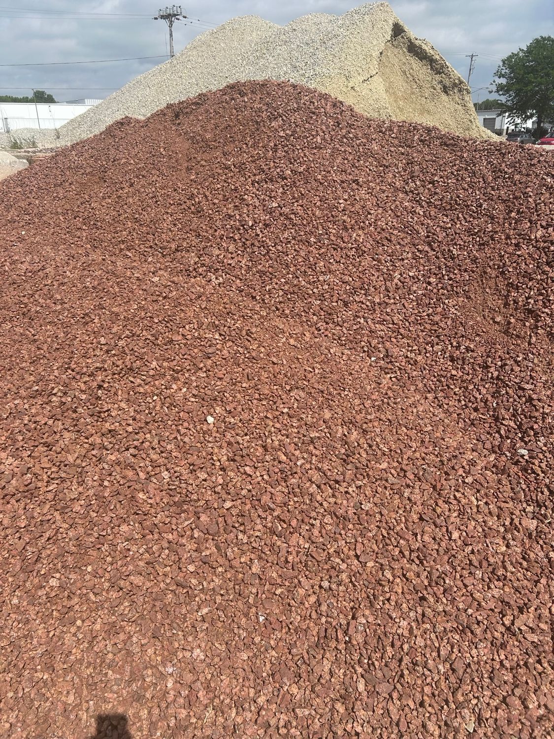 Pile of red gravel in front of a beige gravel pile under a cloudy sky.