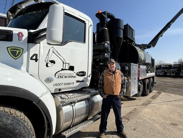 Man standing next to a white vacuum truck with a logo. Sunny outdoor setting.