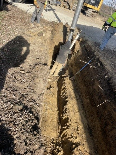 A backhoe digging a trench alongside a road. Construction worker in safety vest.