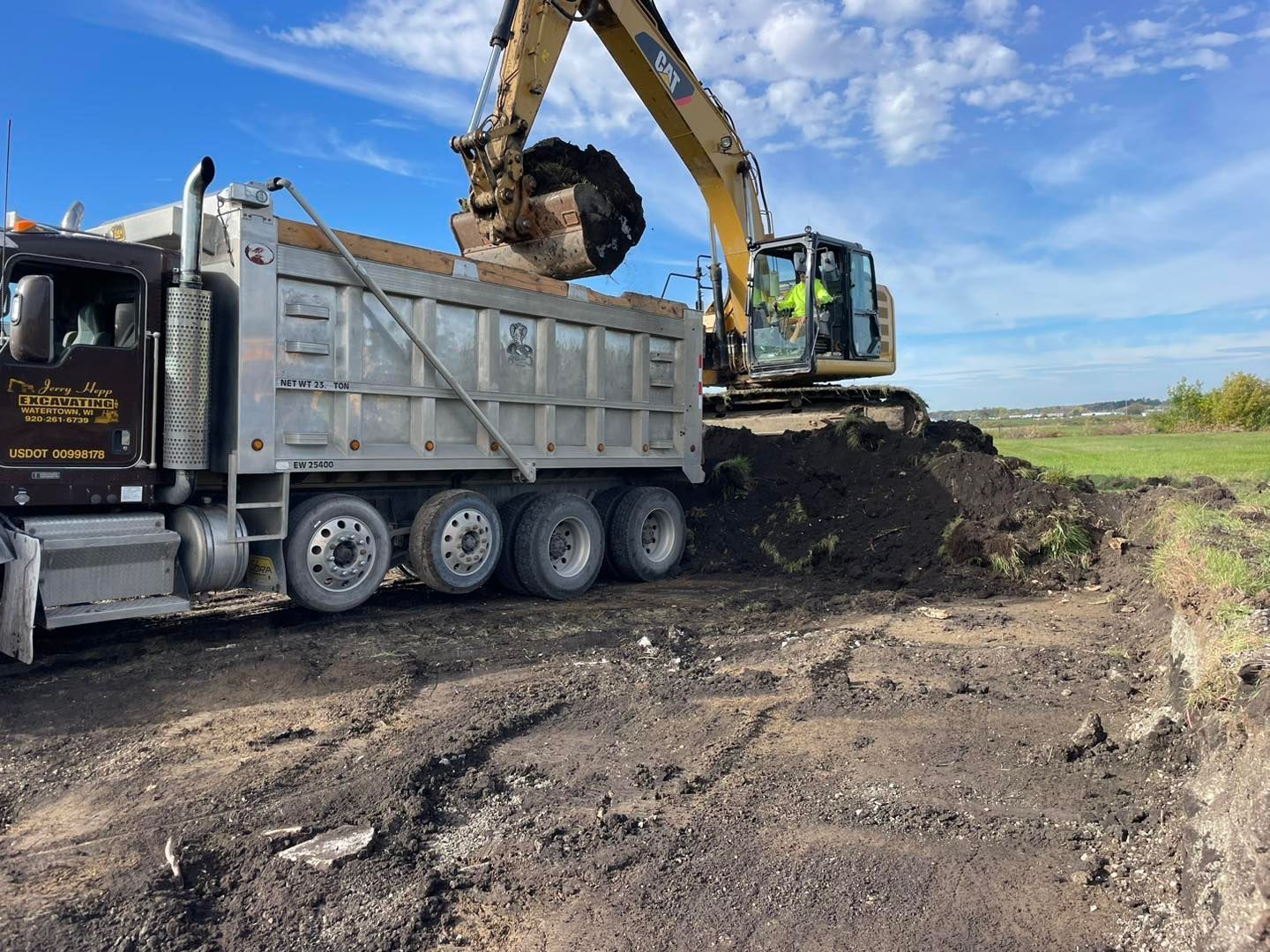 Excavator loading dirt into a dump truck on a construction site under a partly cloudy sky.