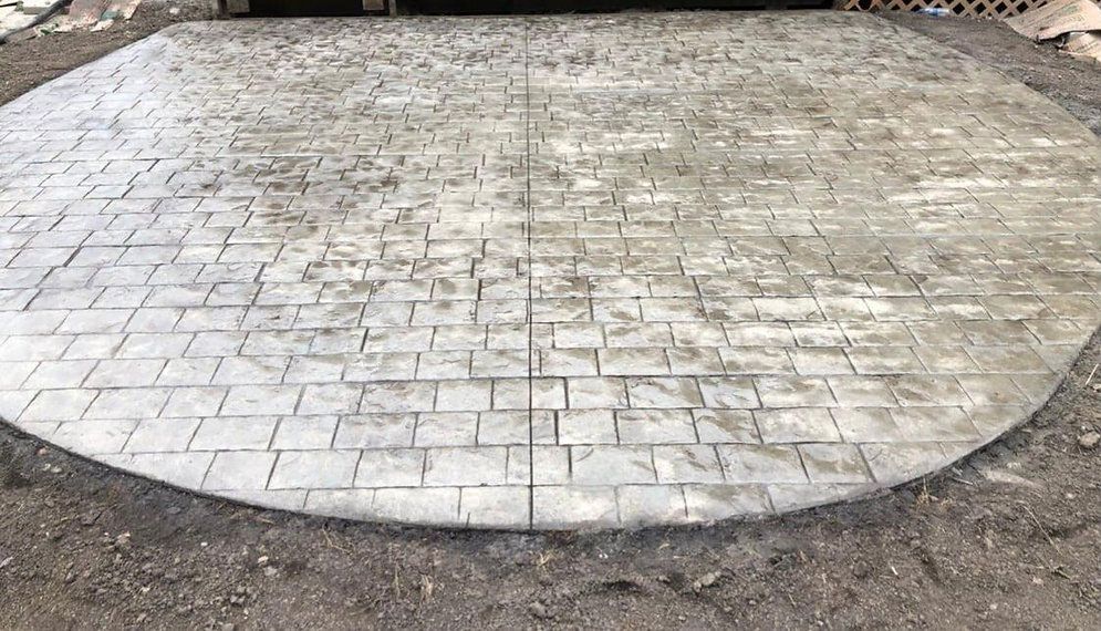 A gray, cobblestone-like concrete patio area in a curved shape, set in dirt.