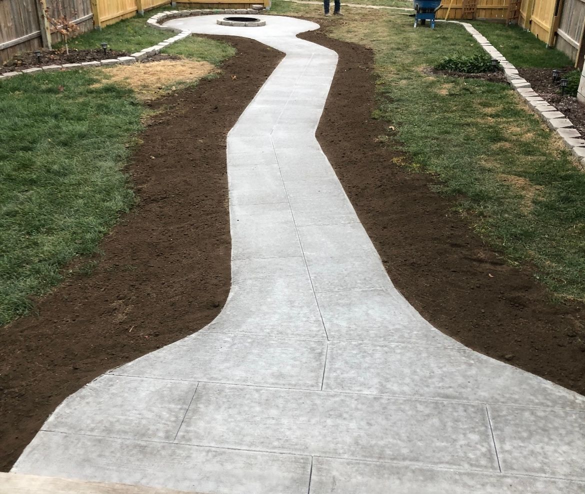 Concrete pathway through a backyard with freshly laid dirt and grass.