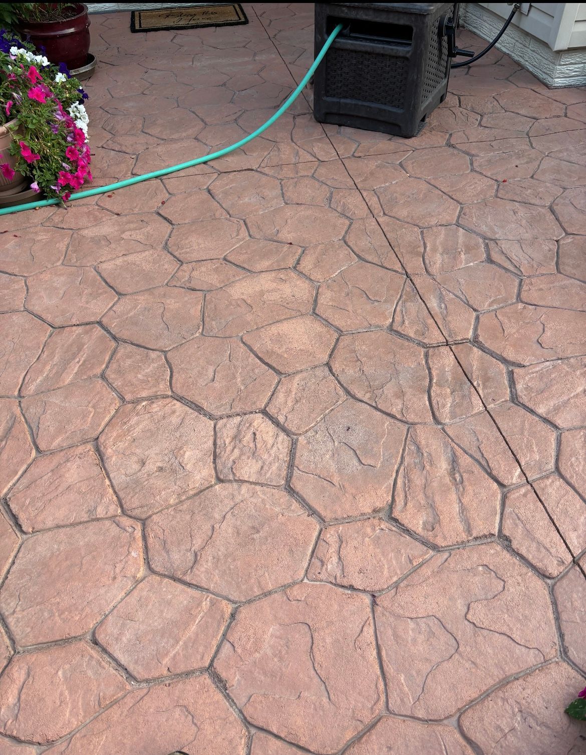 Stamped concrete patio with a hose reel, and potted flowers.
