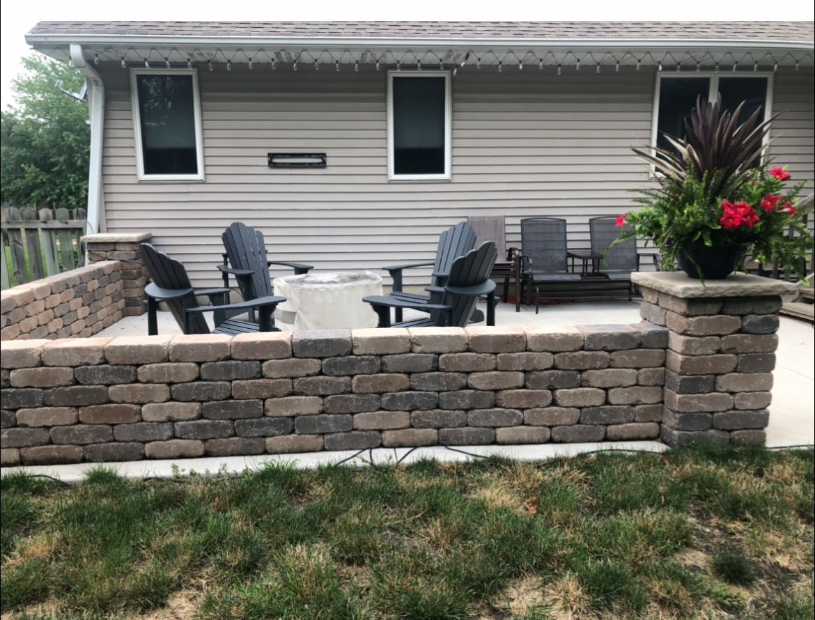 Patio with fire pit, seating, and planter box with flowers, in front of a house.