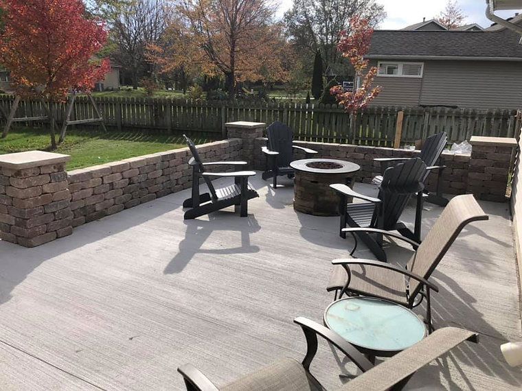 Patio with fire pit and chairs, surrounded by brick walls and a fence, trees in background.