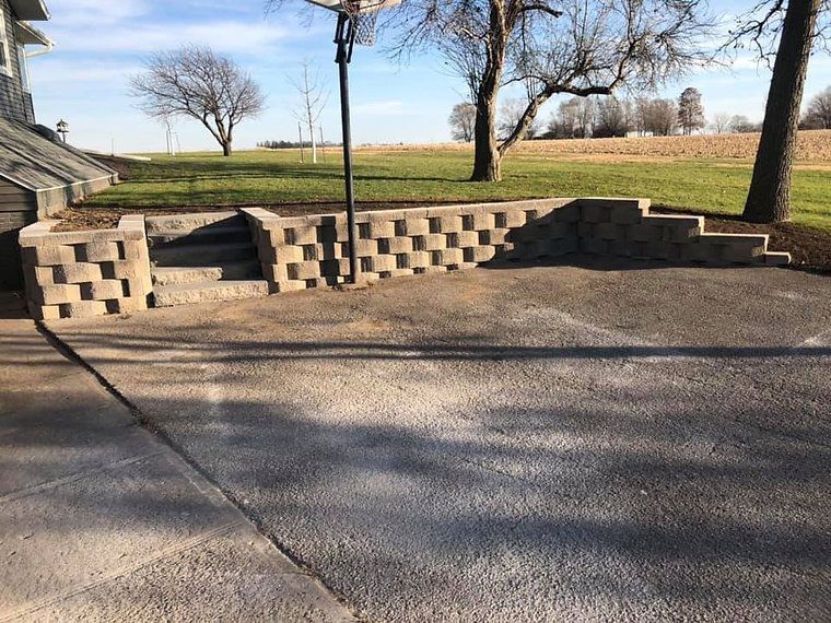 Concrete retaining wall with steps leading to a grassy area, a basketball hoop in the background.