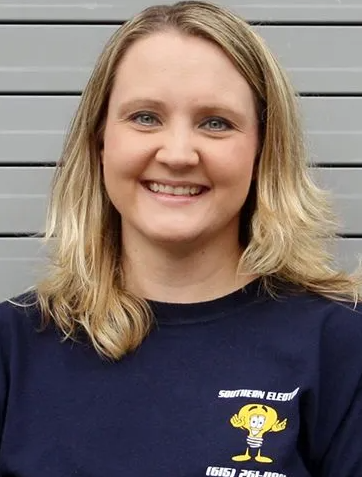 Smiling person in a navy shirt standing in front of a gray wall