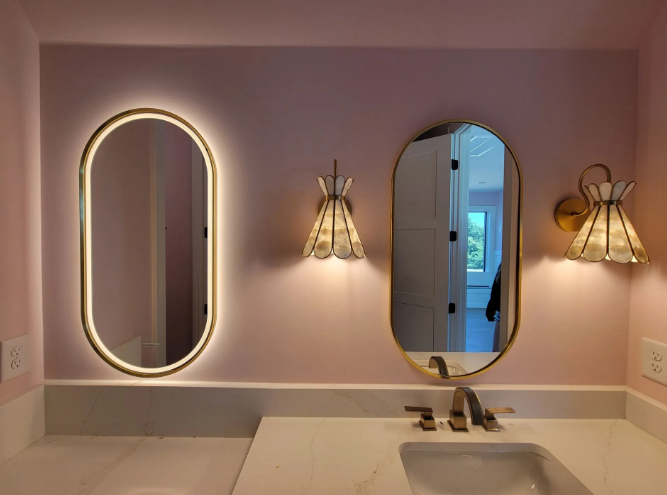 Pink bathroom vanity with two oval mirrors and wall sconces above a sink