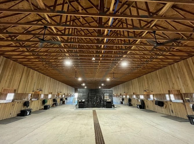 Large wooden barn interior with exposed trusses, lights, and a central aisle leading to a workbench area.