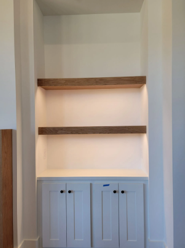 Built-in white alcove with two wooden shelves and cabinet doors below, softly lit from behind
