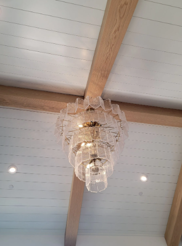 Crystal chandelier hanging from a wood-beamed ceiling with recessed lights