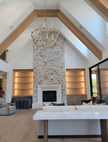 Vaulted living room with stone fireplace, exposed beams, and a gold chandelier above a white sofa.