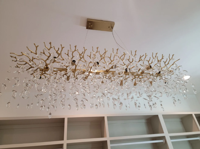 Gold branch-style chandelier hanging from a ceiling above white shelving units