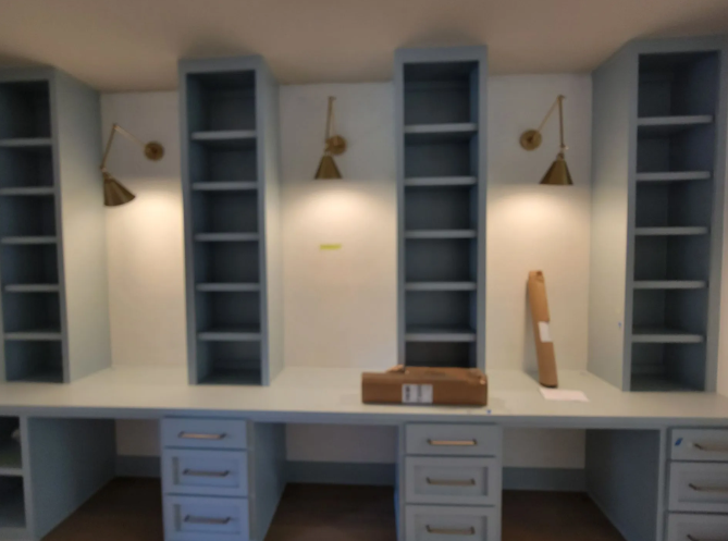 Blue built-in desk with shelving and drawers, featuring brass wall lamps and small decor in a white room.