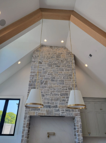 Stone fireplace with vaulted white ceiling and wood trim in a bright room