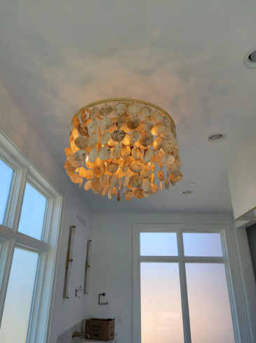 Chandelier with golden leaf-like shades on a white ceiling in a bright room with windows