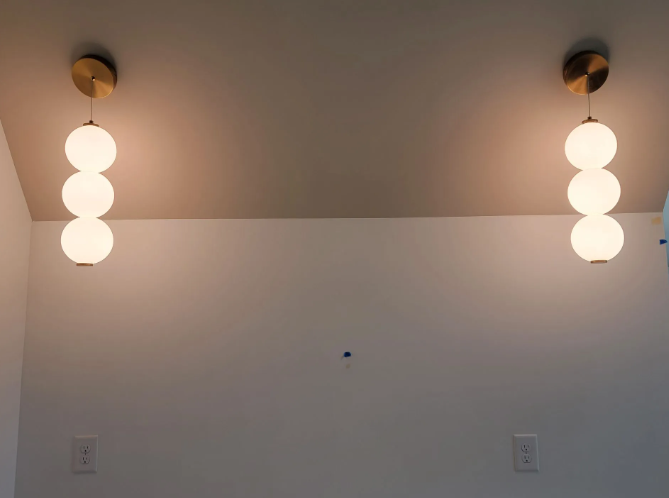 Two modern pendant lights flanking a blank wall above a white lower wall.