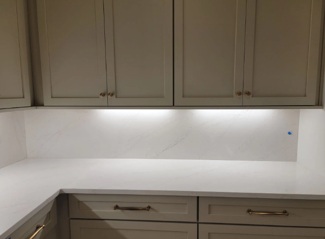 Empty kitchen counter with beige cabinets and white backsplash under under-cabinet lighting