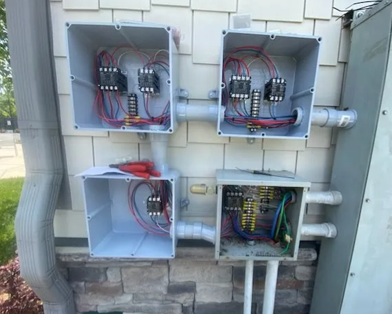 Open electrical panels with wiring and circuit breakers mounted on an exterior wall.