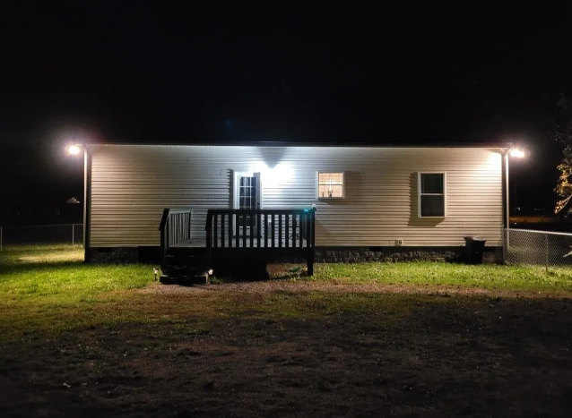 Single-story house at night, lit by porch lights with a small front deck and grassy yard.