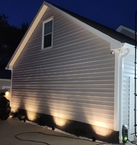 Lit white house siding at night with ground lights illuminating the side wall