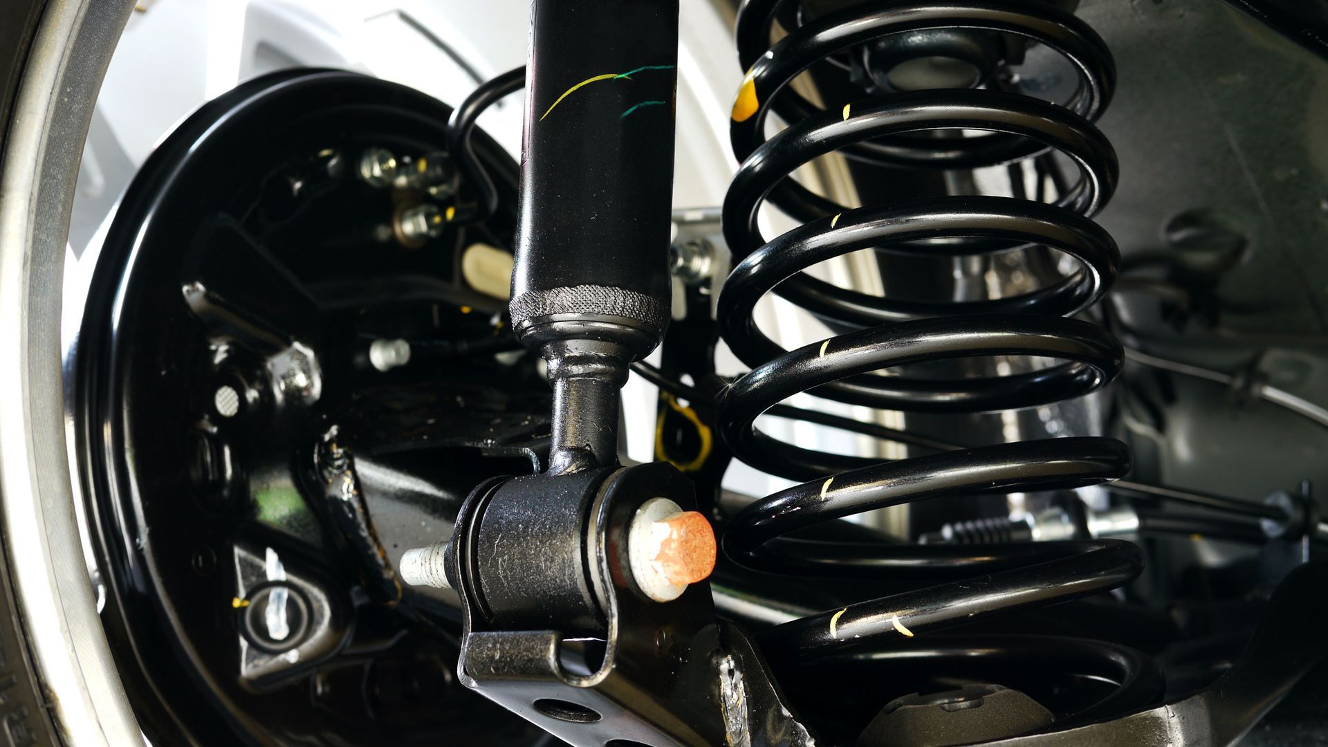 A close-up view of a car’s rear suspension system, featuring a black coiled spring and a shock absorber mounted to the frame.