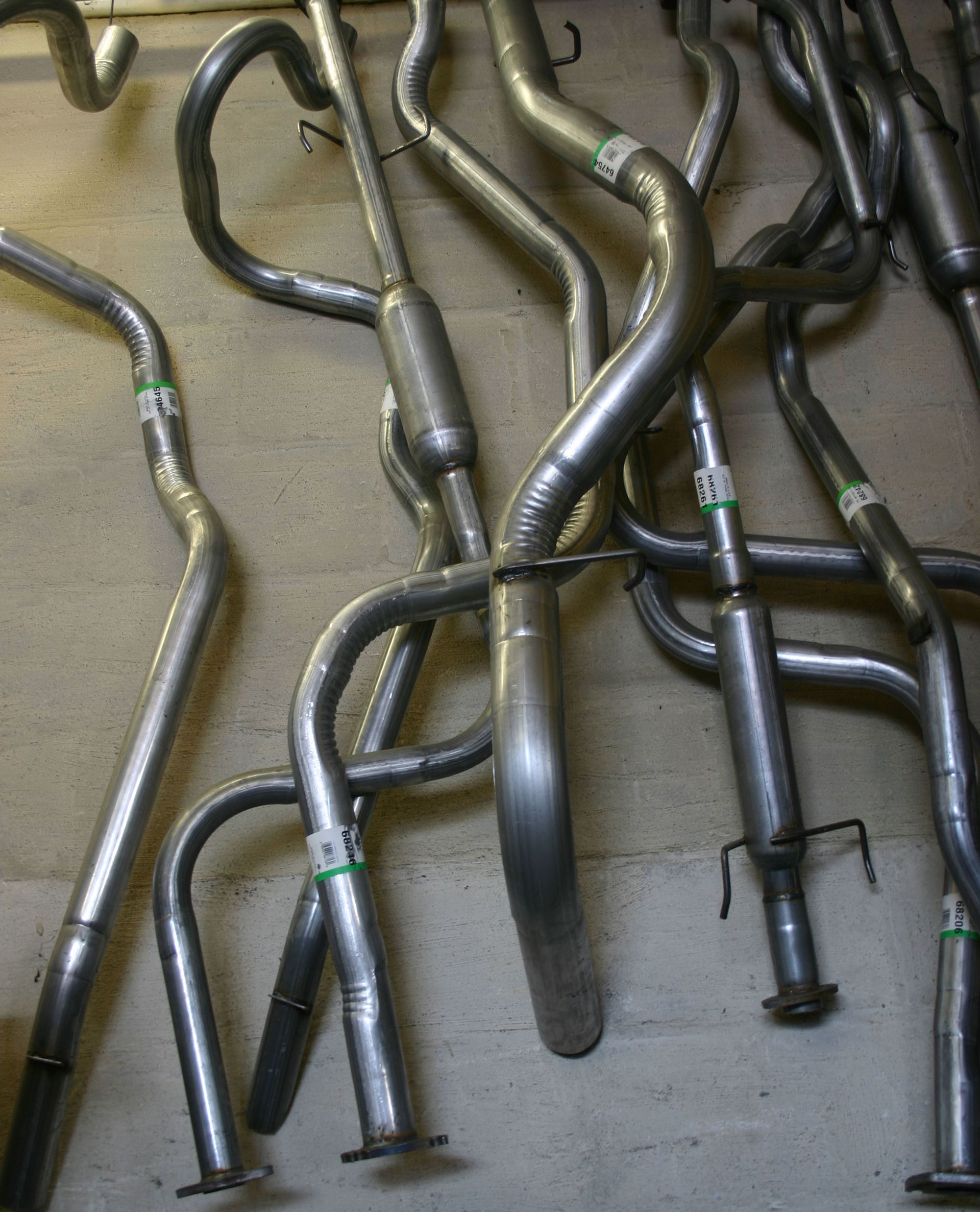 A collection of various metal automotive exhaust pipes and tubes laid out on a concrete floor.