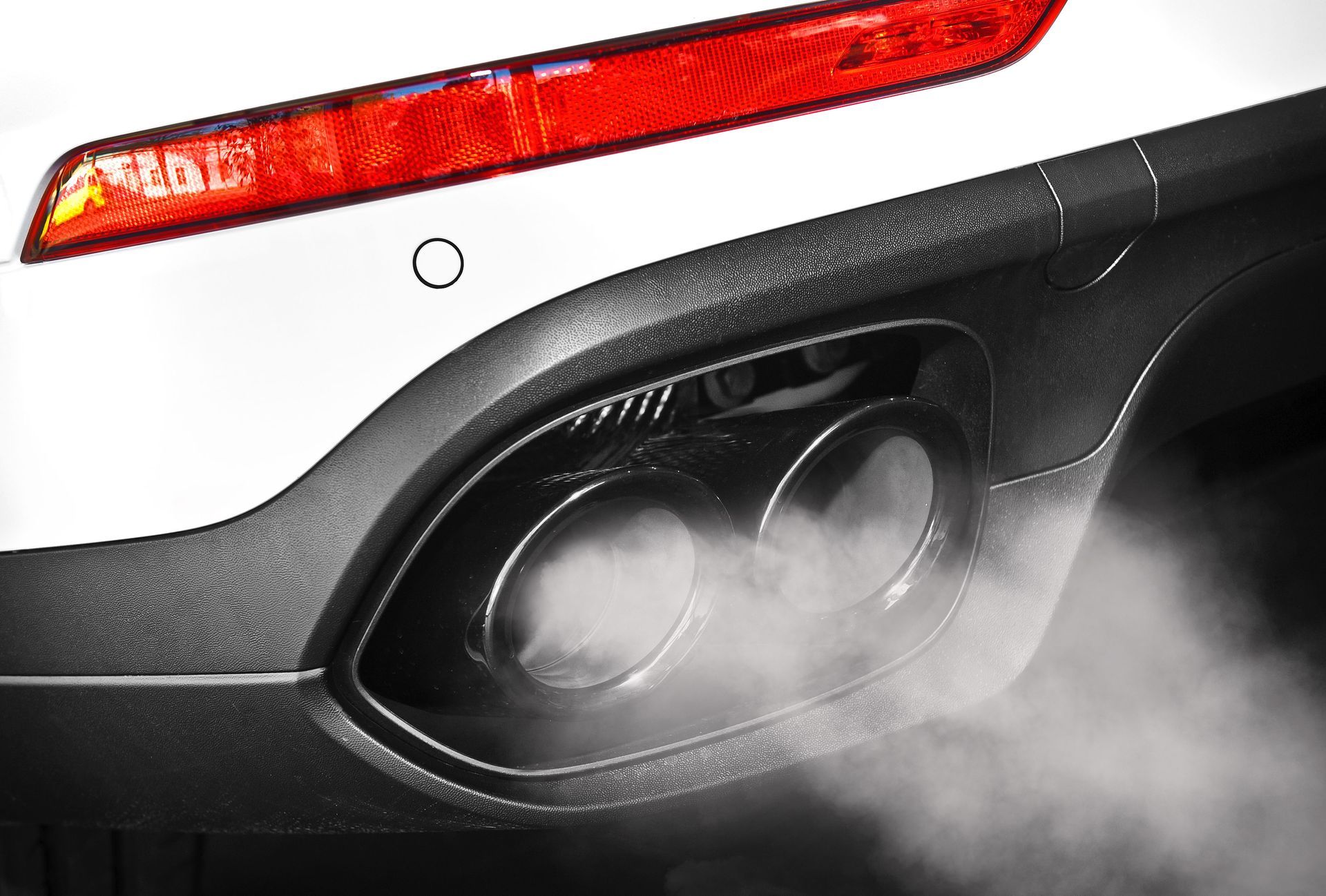A close-up of a white car's dual exhaust pipes emitting a thick cloud of white exhaust smoke.