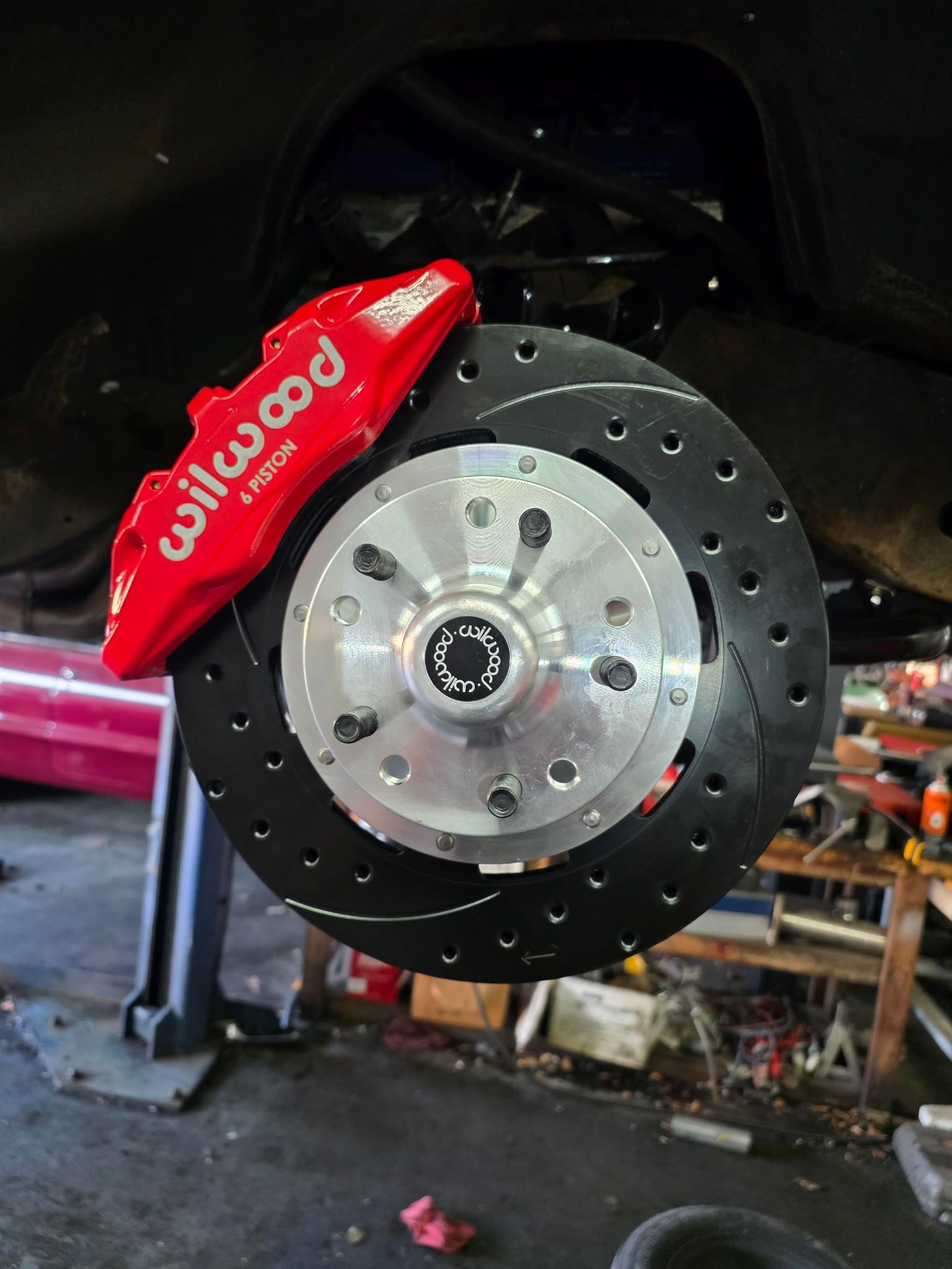 Red brake caliper on a drilled car brake disc in a garage, mounted on a black suspension assembly