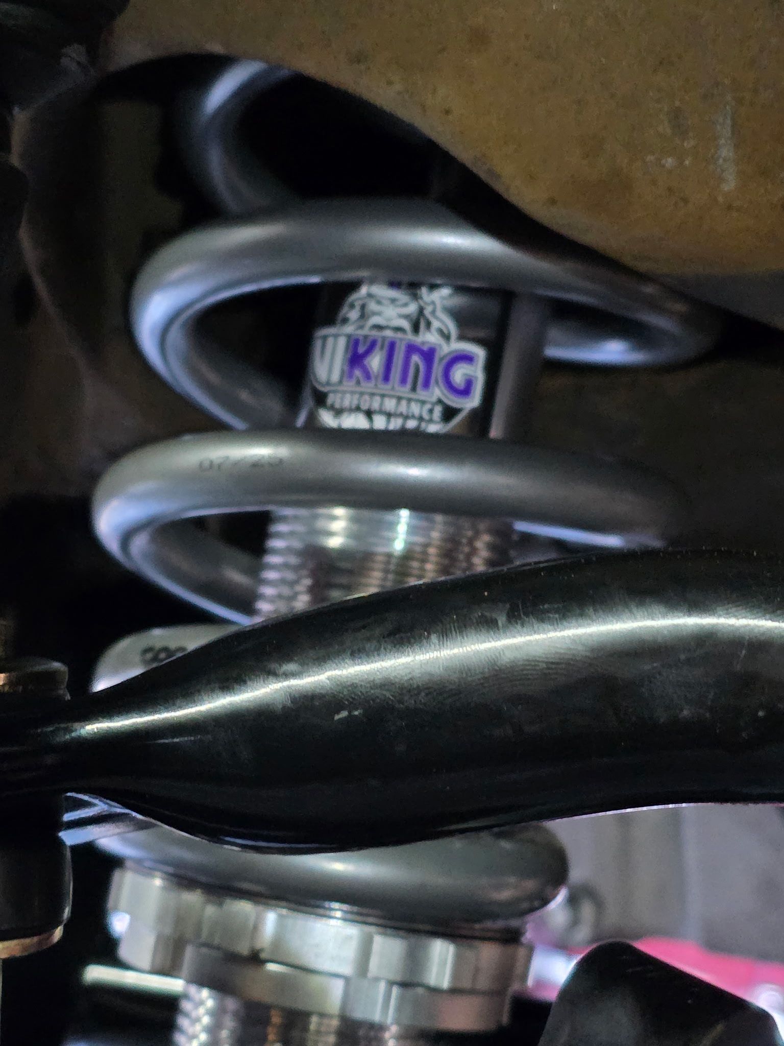 Close-up of a silver suspension spring with a black control arm and a KING shock absorber label.