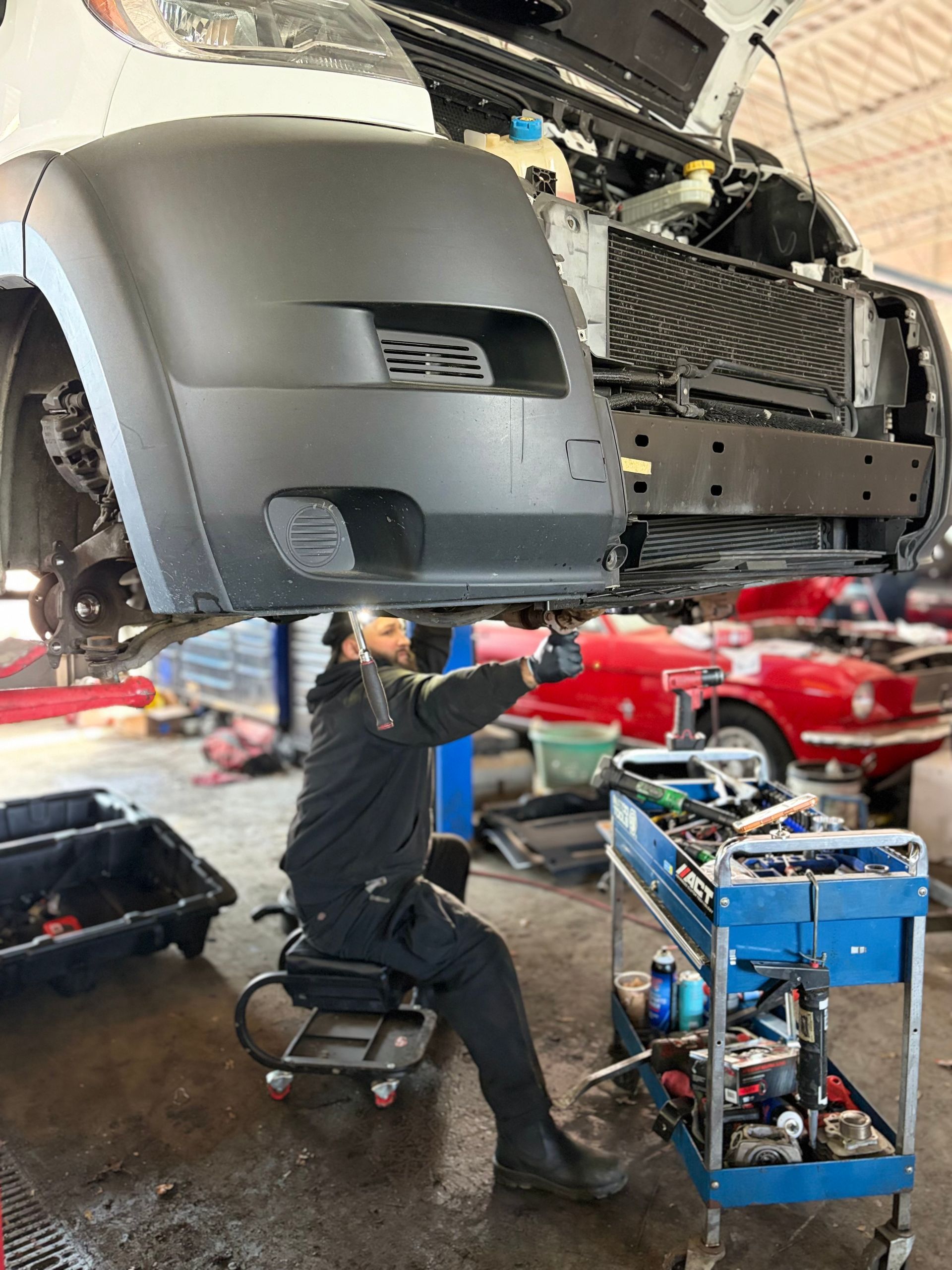 Mechanic working under a lifted car in an auto repair shop, with tools and a cart nearby