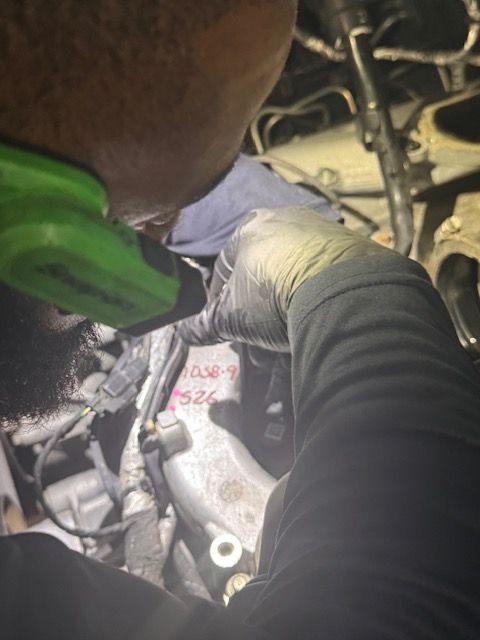 A worker in a dark uniform uses a yellow tape measure to check a bent metal pipe on a blue industrial workbench.