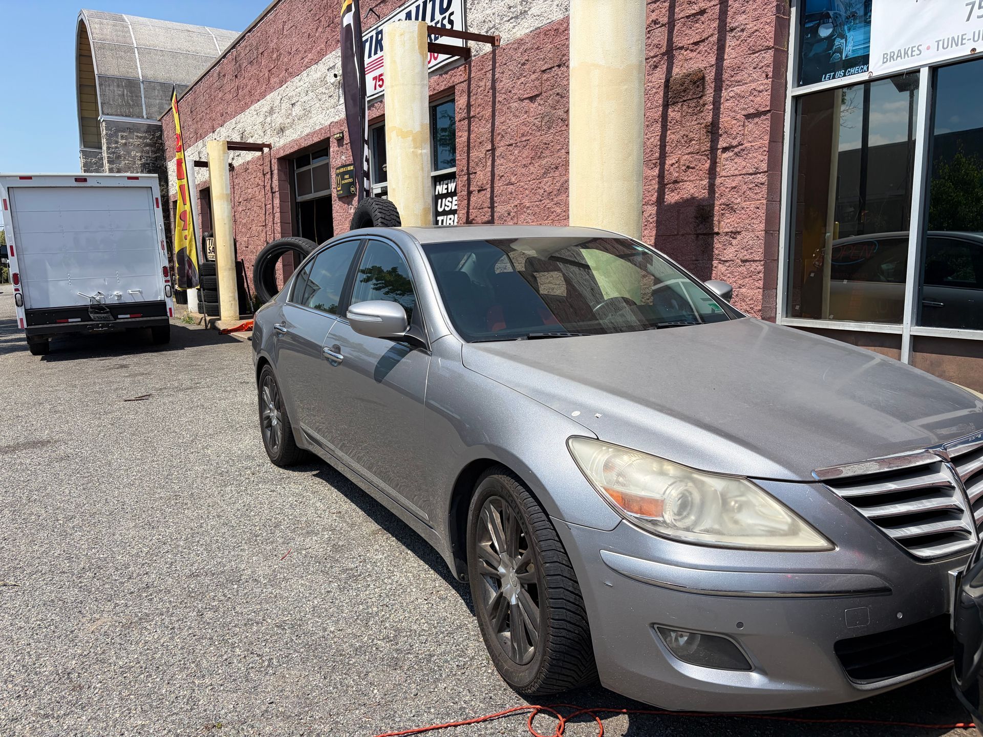 Silver sedan parked beside a brick building with a white truck in the background