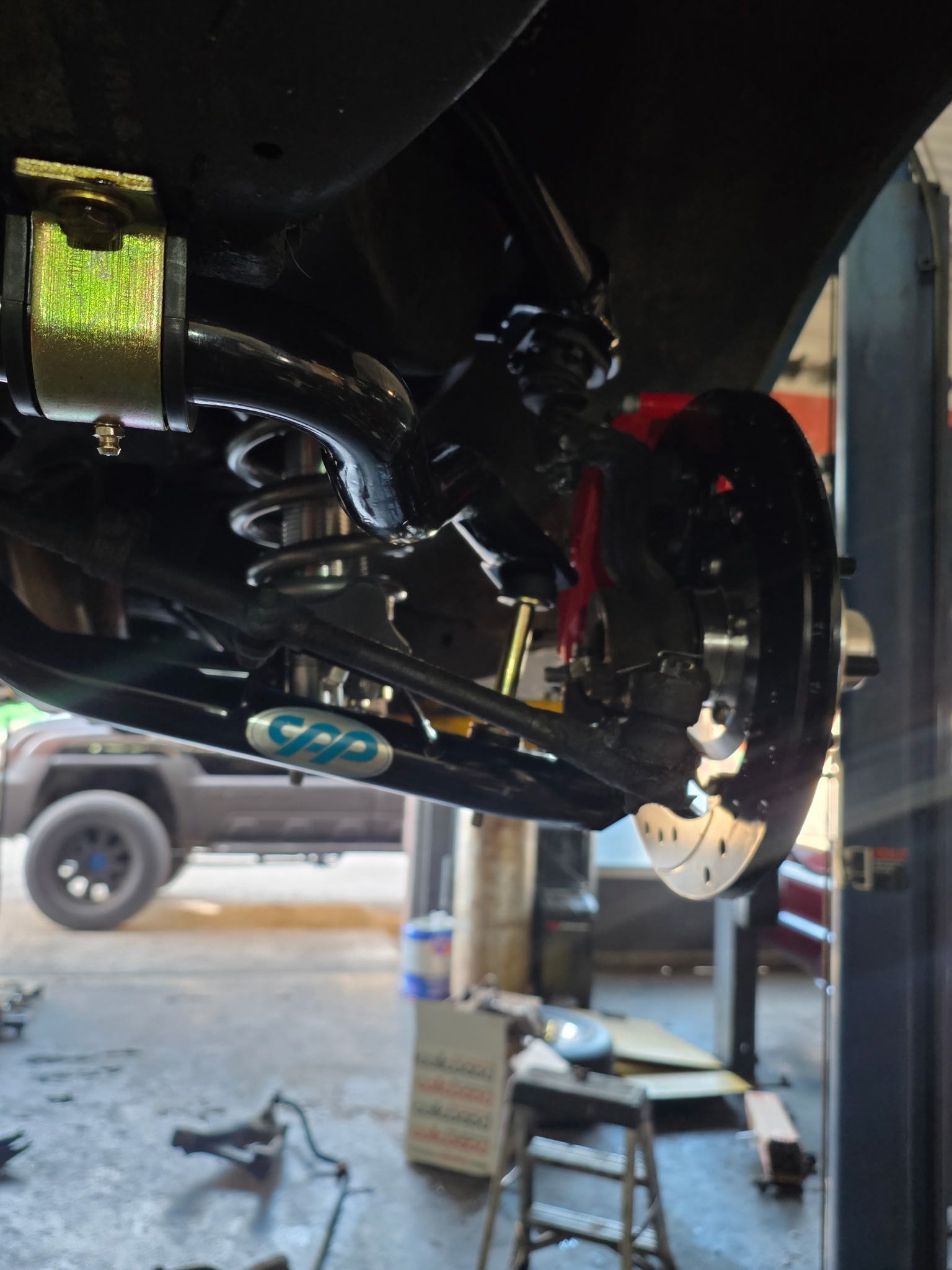 Undercarriage of a lifted vehicle in a garage, showing suspension and brake components during repair