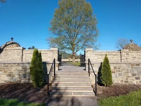 Stone steps leading to a gate and path, flanked by walls and trees, against a blue sky.