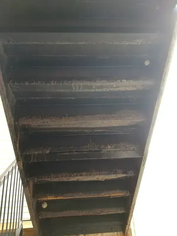 Underside view of wooden outdoor stairs with weathered planks and black railings.