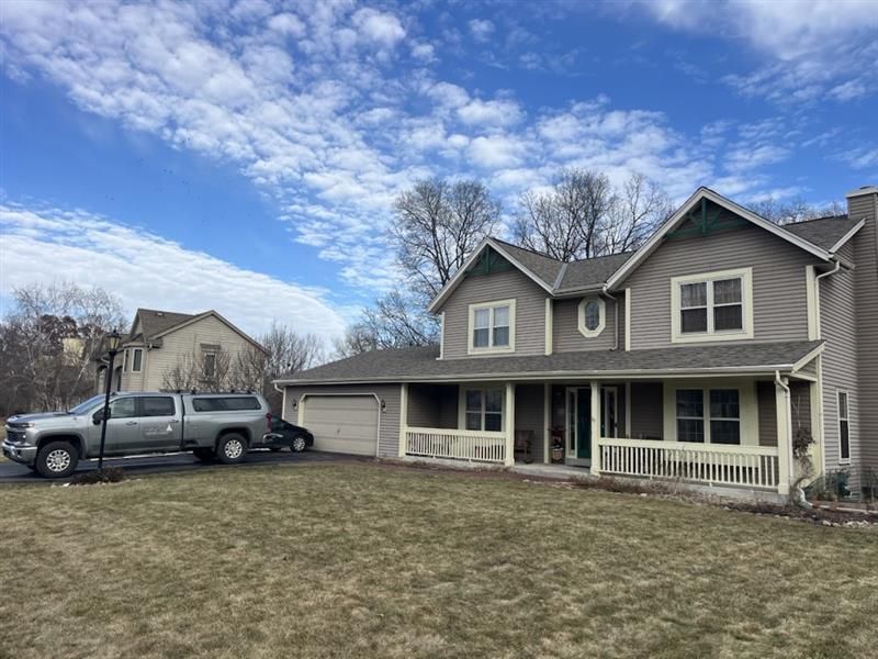A two-story gray house with a porch and a pickup truck parked in the front yard on a cloudy day.