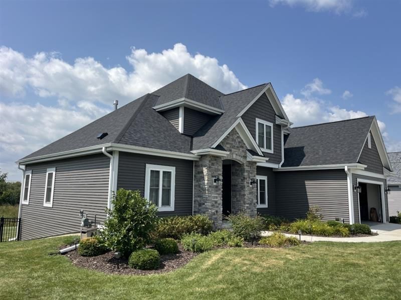 Gray house with a dark roof, white trim, and stone accents under a blue sky.