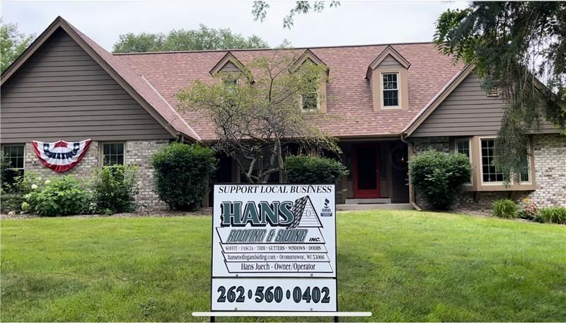 House with brown roof and siding; sign in front advertising 