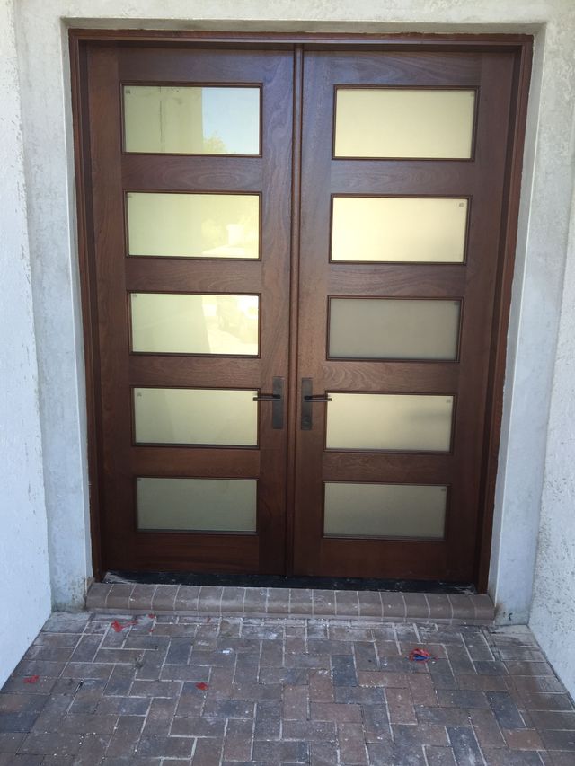 Brown double doors with frosted glass panels at a building entrance, viewed from outside.