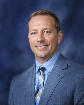 Man in a blue plaid suit smiles at the camera against a blue background.