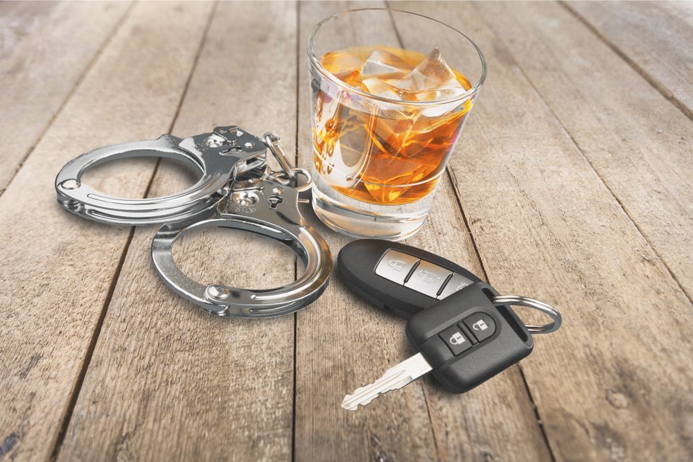 Handcuffs, car keys, and a glass of amber liquid with ice on a wooden surface.
