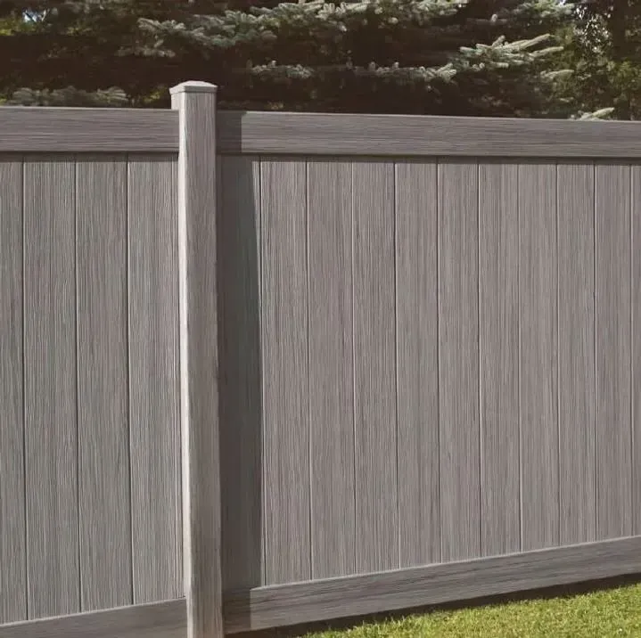 A gray wood-grain texture privacy fence with a matching vertical post against a background of pine tree branches.